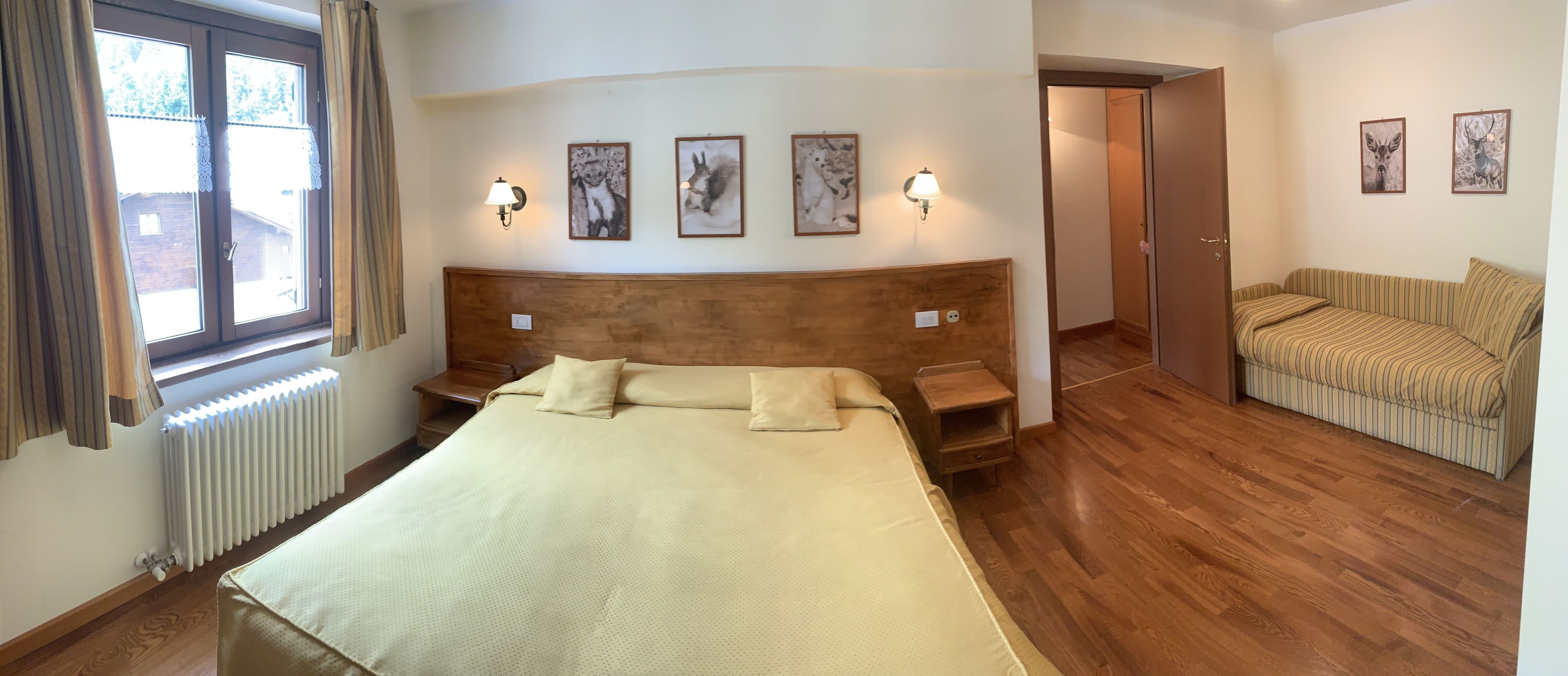 A hotel room with a large bed, wooden headboard, two wall-mounted lamps, and a window with curtains.