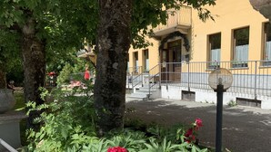 En gårdhave med blomstrende planter, en gul bygning med balkon og gelænder.