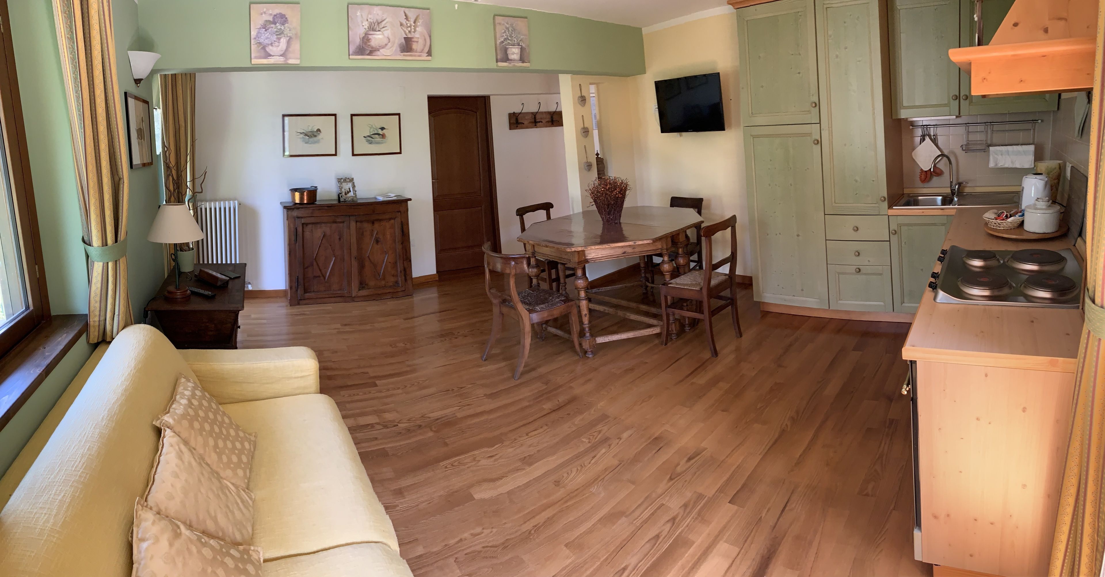 Un salon confortable avec un canapé, une table à manger avec des chaises, un coin cuisine doté de placards et d’une cuisinière, et un téléviseur fixé au mur.