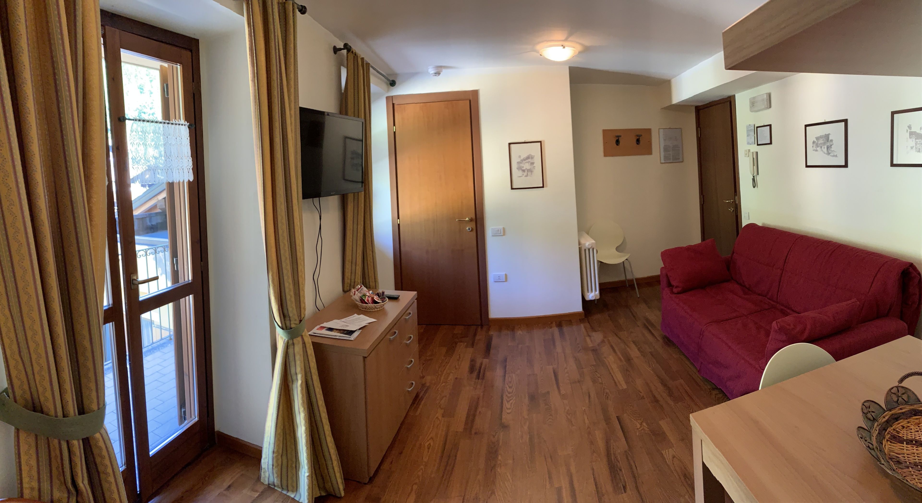 Una habitación acogedora con piso de madera, un sofá rojo, un escritorio de madera y un televisor en la pared.