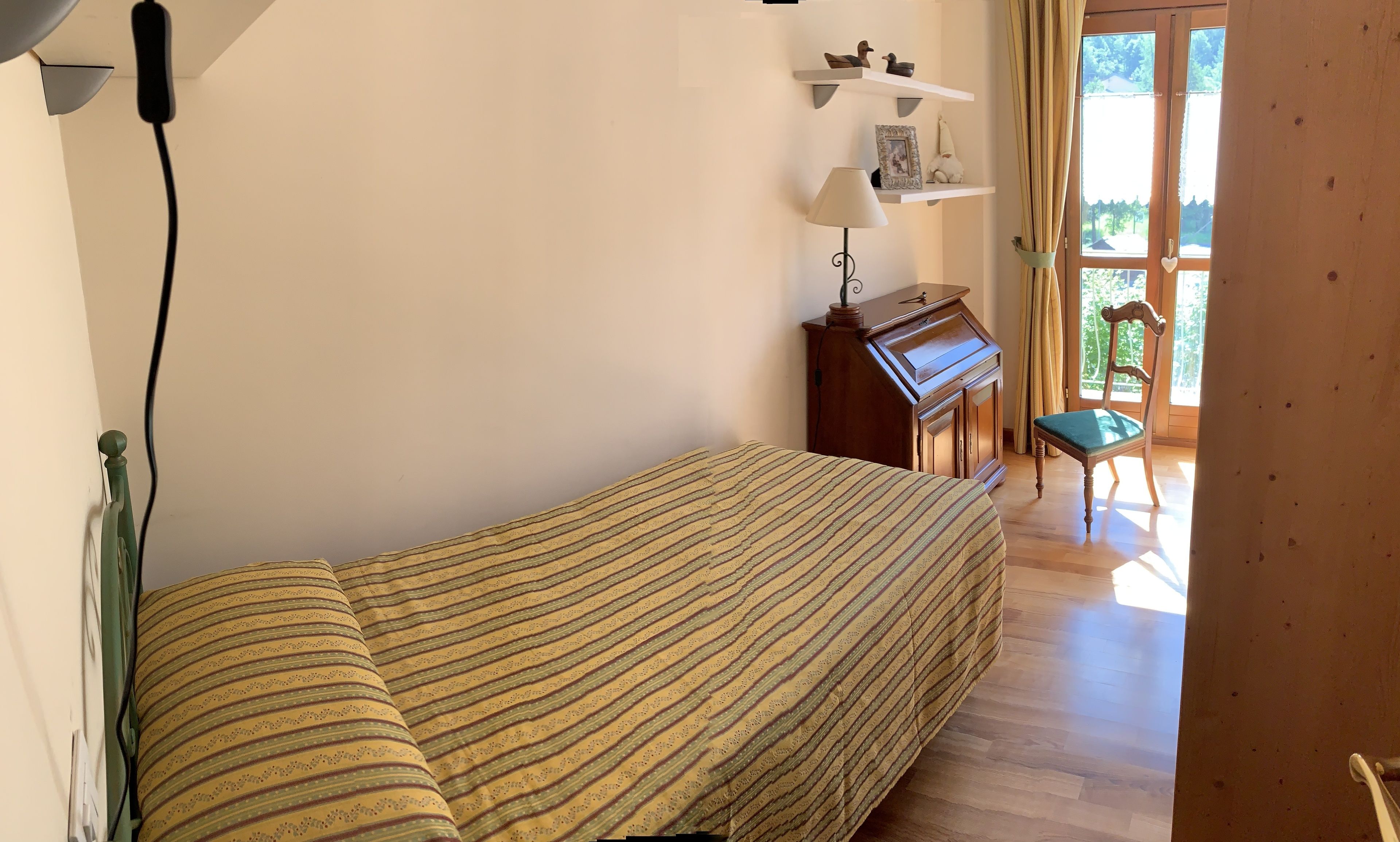 A bedroom with a bed, a desk with a lamp, a chair, and a piano.