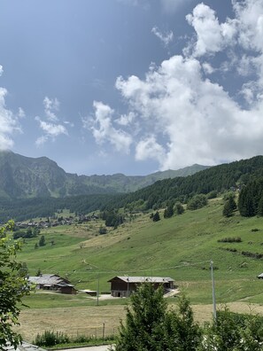 A rural landscape with green fields, a few buildings, and mountains in the background.