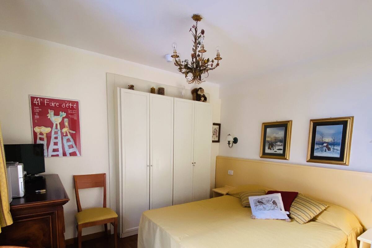 A bedroom with a bed, a desk, a chair, a wardrobe, and a chandelier.
