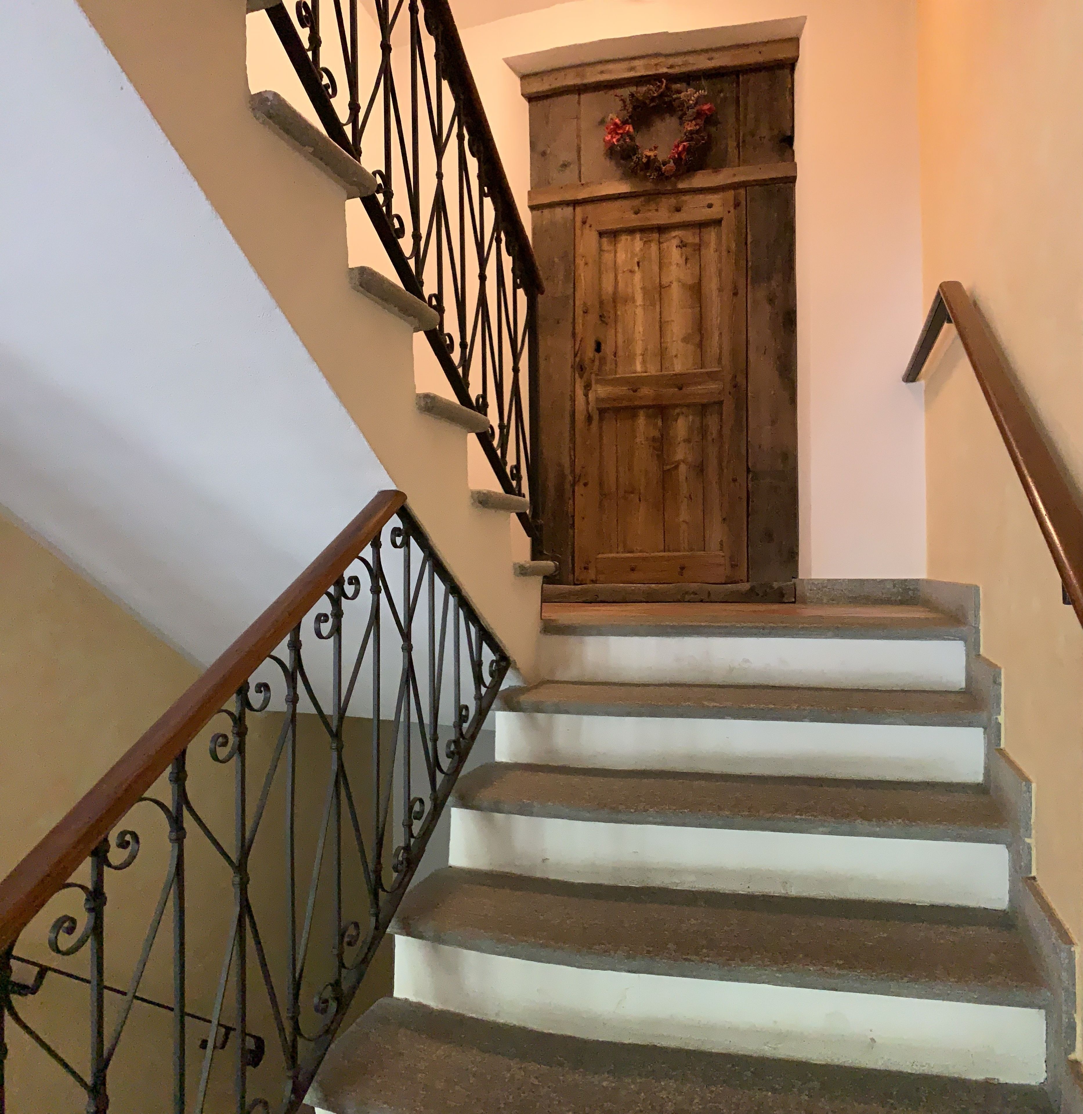 A wooden staircase with a metal railing and a door with a wreath.