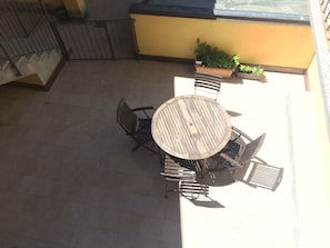 An outdoor patio with a round wooden table and chairs, surrounded by potted plants.