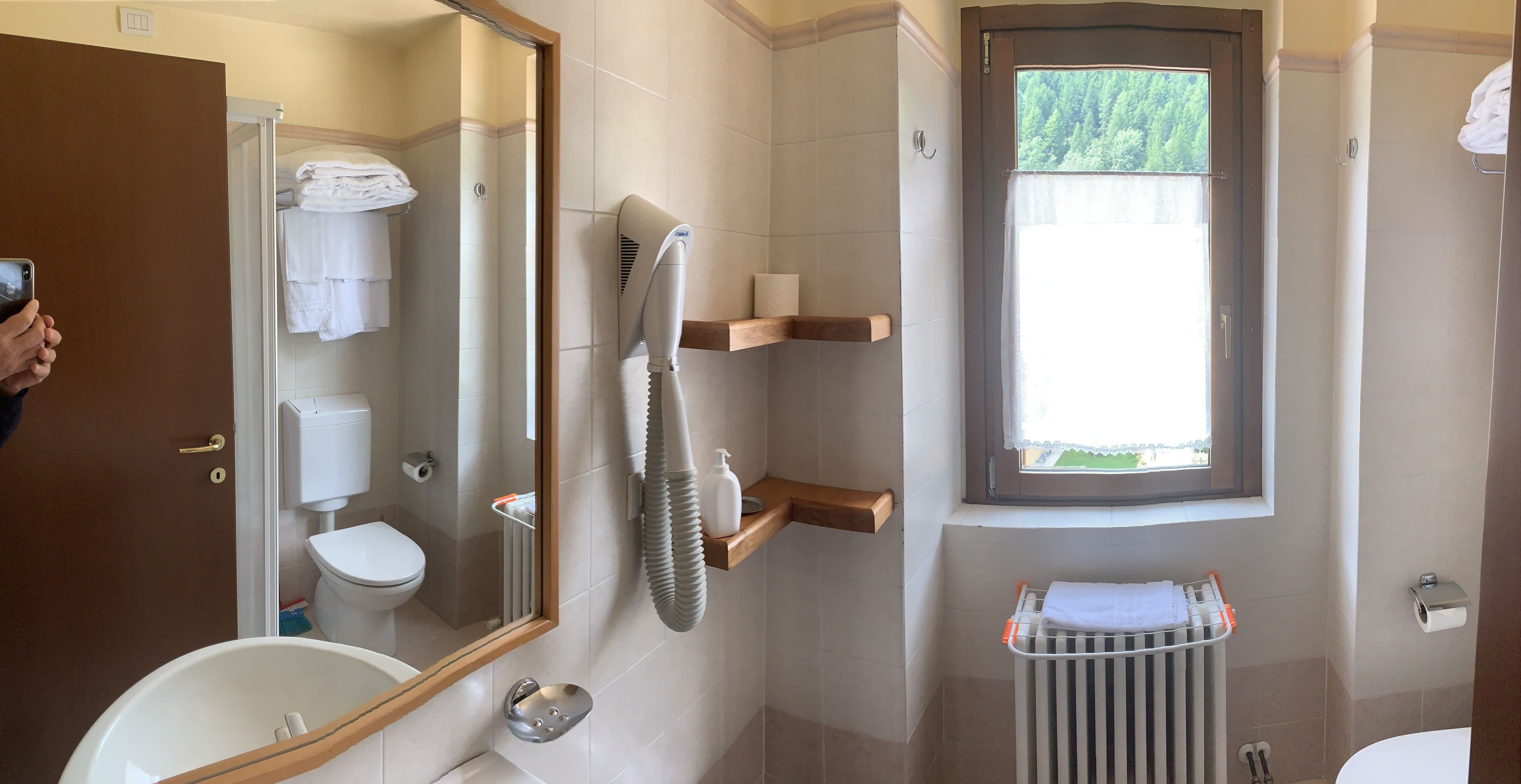 A bathroom with a toilet, sink, mirror, towel rack, and a window.