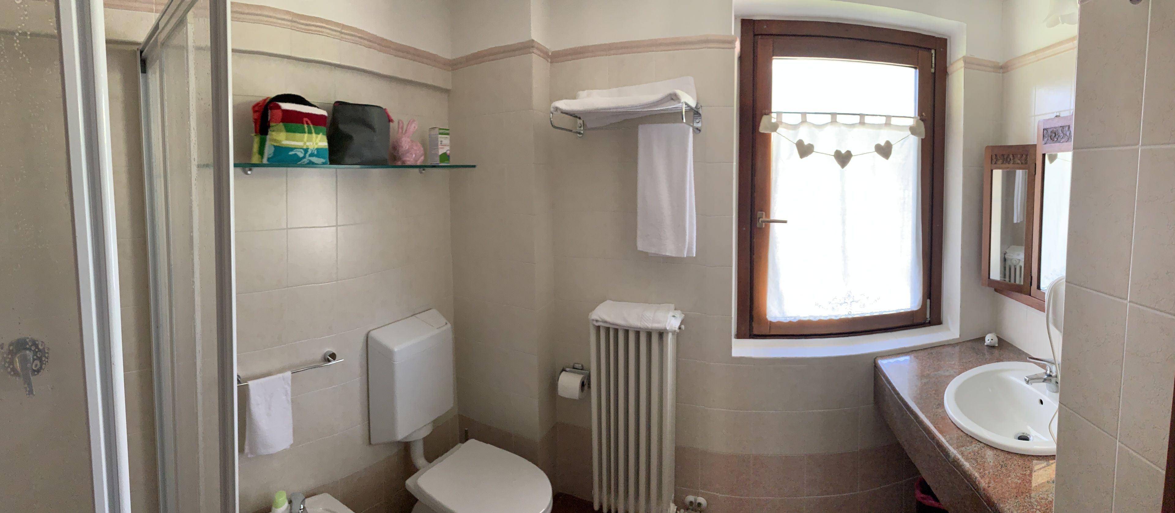 Un baño con inodoro, lavamanos, ducha y ventana con cortina.