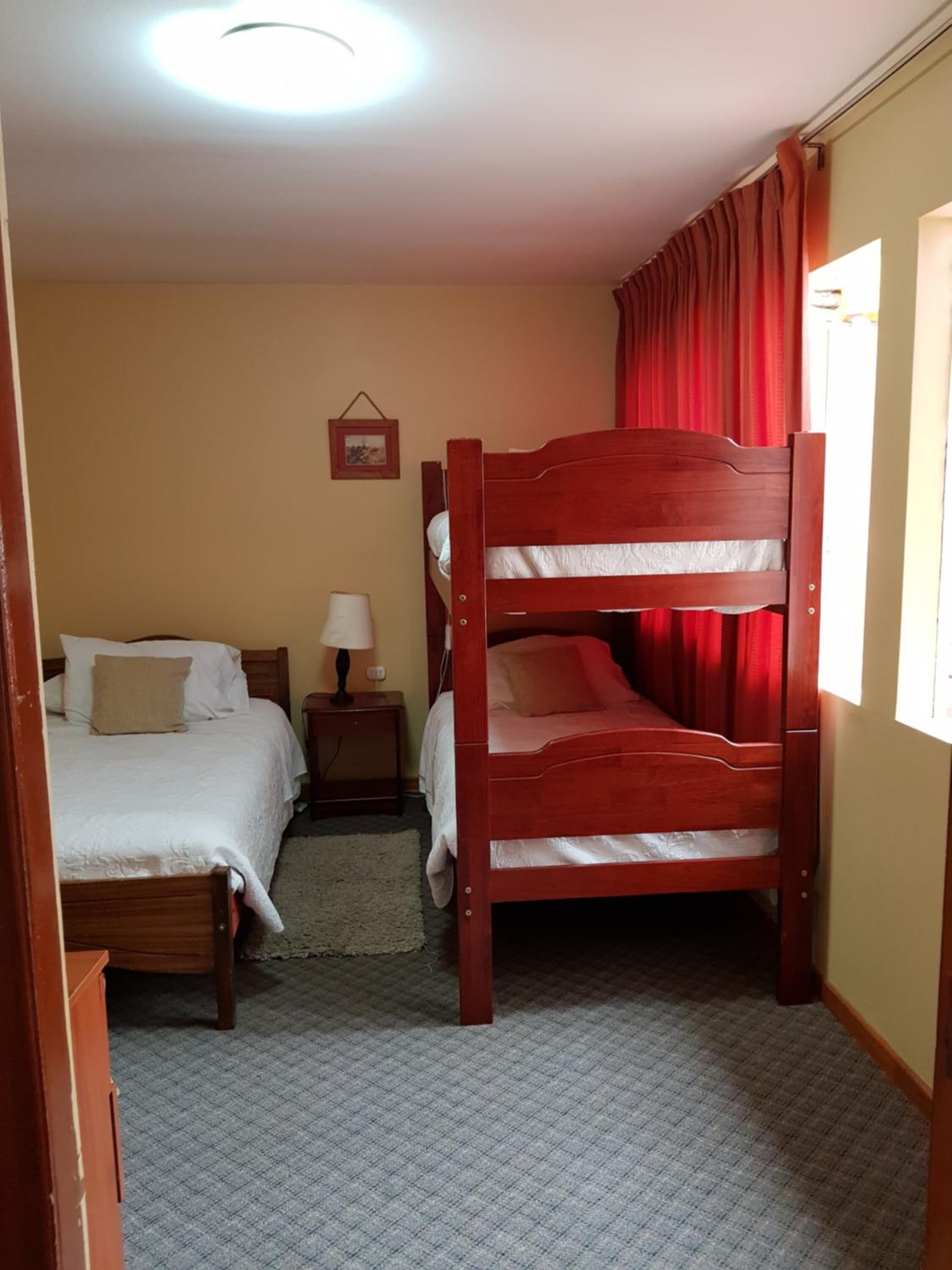 Ein Zimmer mit einem Etagenbett, einem Einzelbett, einem Nachttisch mit Lampe und einem gerahmten Bild an der Wand.