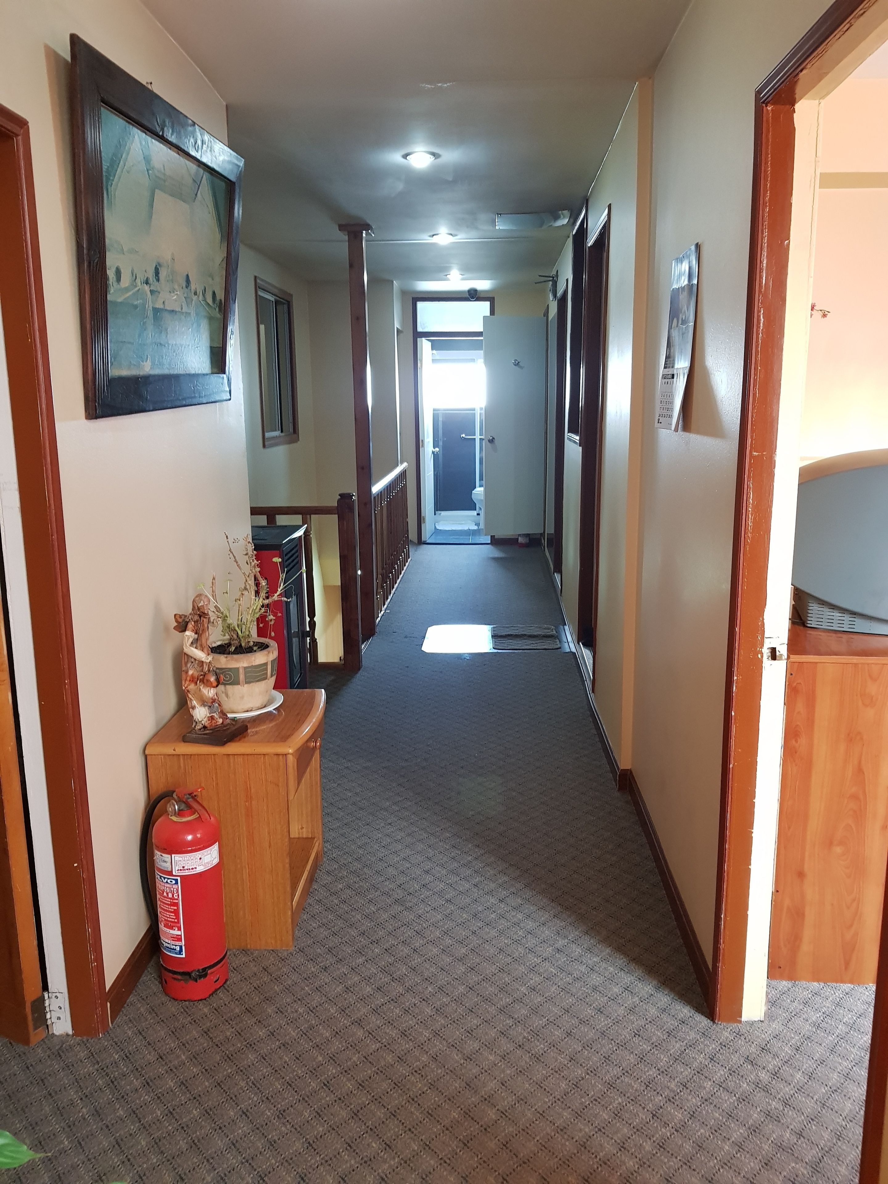 A hallway with a fire extinguisher, a wooden bench, and a potted plant.