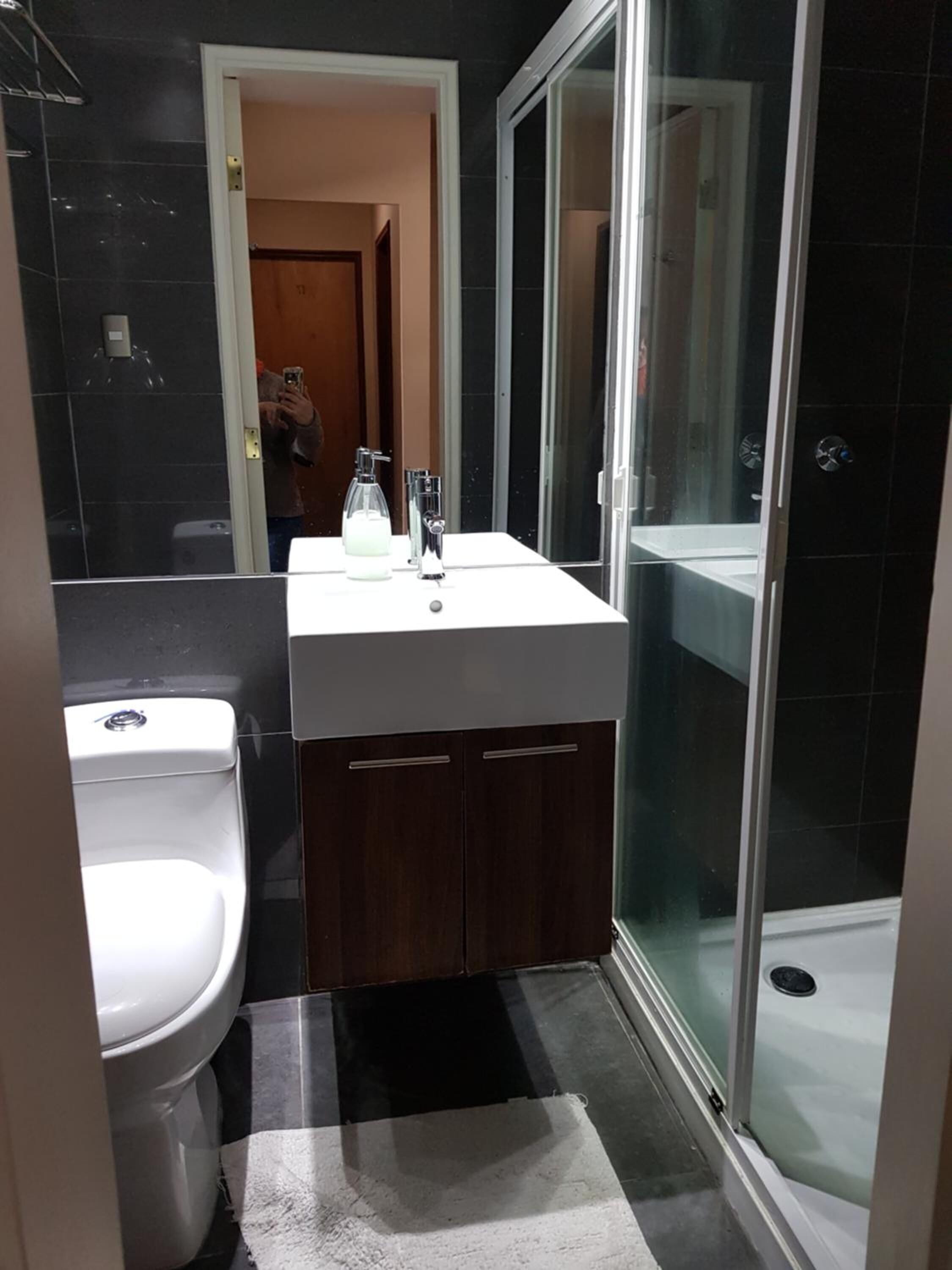 Un baño pequeño con inodoro blanco, lavamanos con espejo y cabina de ducha de cristal.