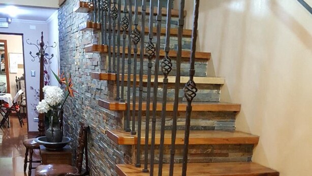Eine Holztreppe mit Metallgeländern führt zu einer Zwischenebene mit einem Blumenvasen und einem Stuhl.