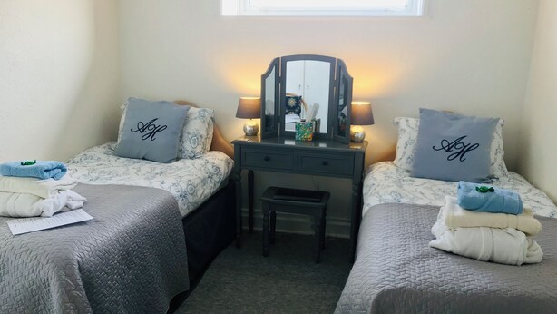 A twin bedroom with two beds, a desk, a chair, and a window. - Arden House (Arundel)