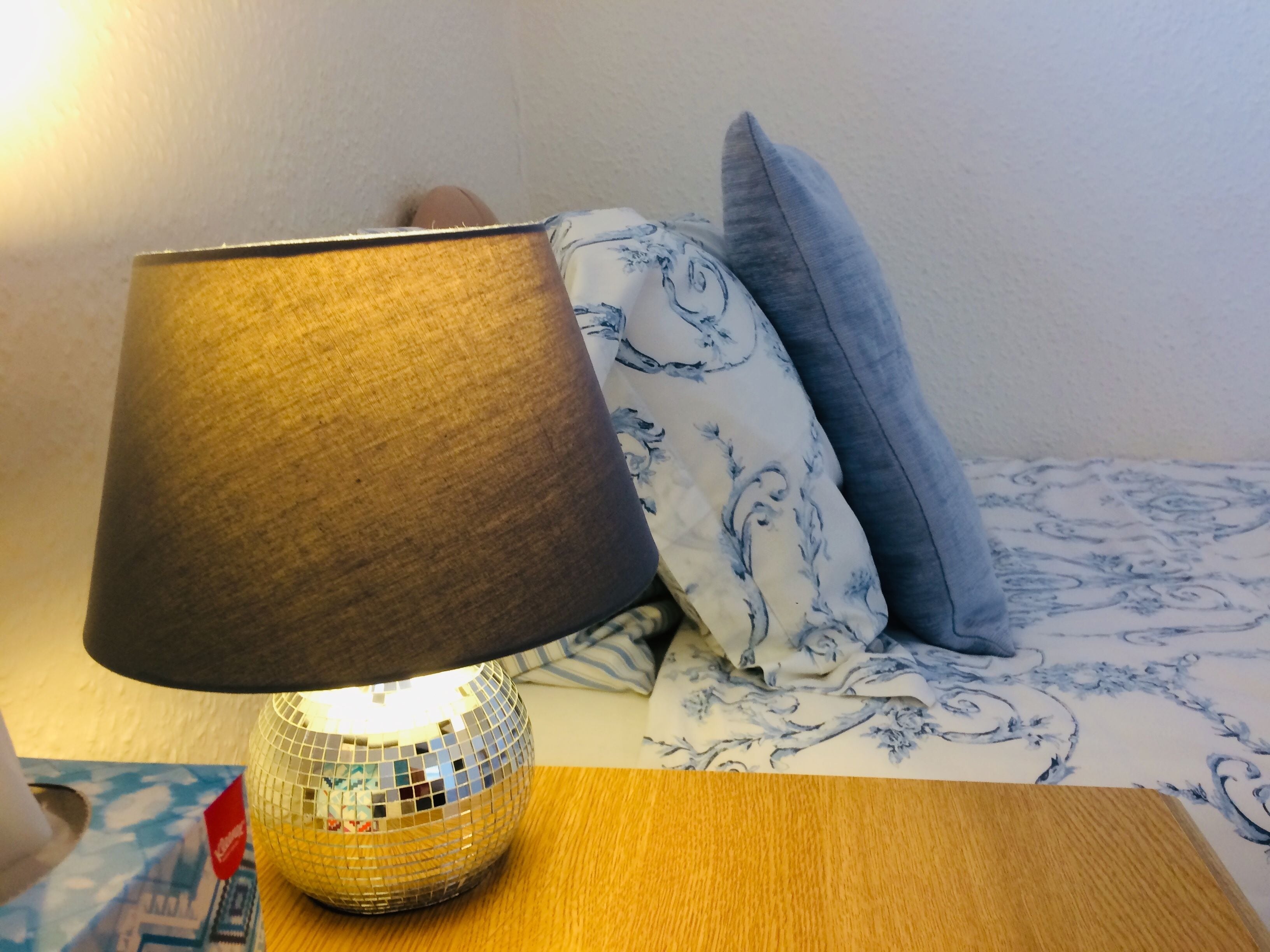 A bedside table with a disco ball lamp, a patterned pillow, and a floral bedspread.