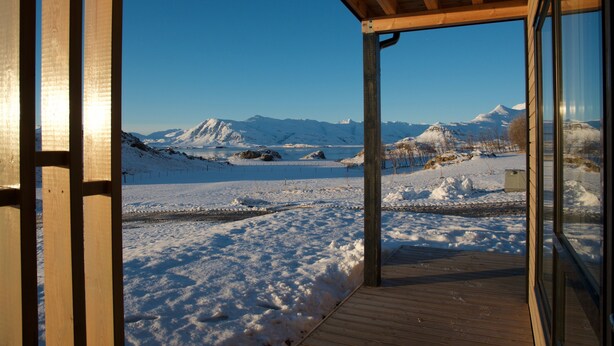 Una terraza de madera que conduce a una puerta de vidrio con vistas a montañas nevadas.