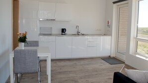 Una cocina moderna con armarios blancos, una mesa de comedor con una silla y una cafetera.