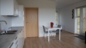 Una cocina moderna con armarios blancos, una puerta de madera, una mesa de comedor con dos sillas y una planta en maceta.