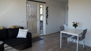 Una sala de estar moderna con un sofá oscuro, una mesa blanca y una puerta que da al exterior.