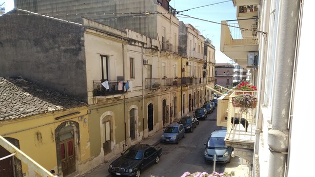 Una calle estrecha bordeada de coches aparcados y edificios con balcones.