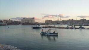 Una marina con barcos amarrados, un litoral rocoso y edificios al fondo.