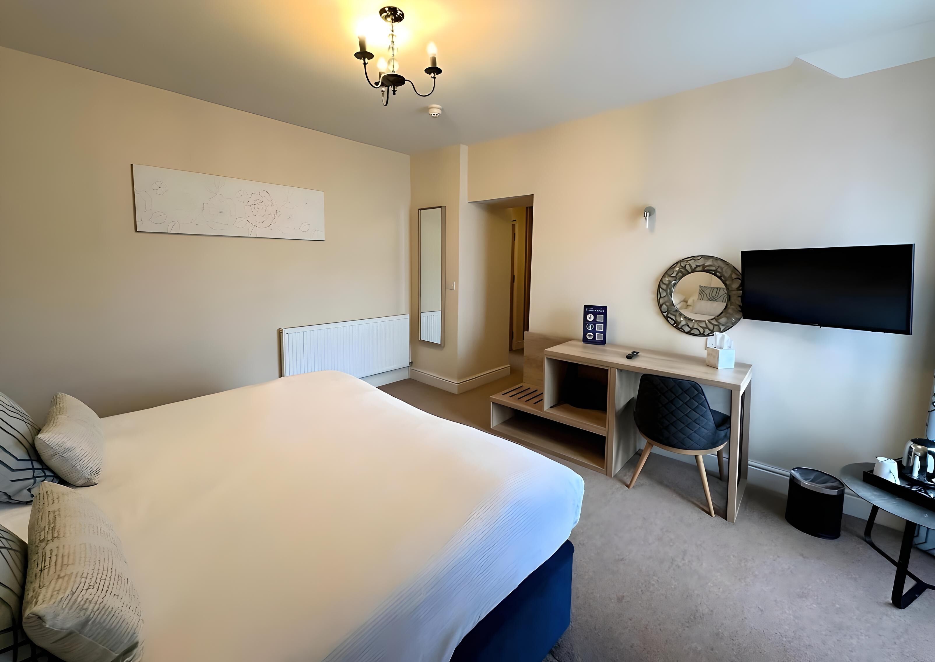 Hotelkamer met een groot bed, bureau met stoel, televisie en spiegel.