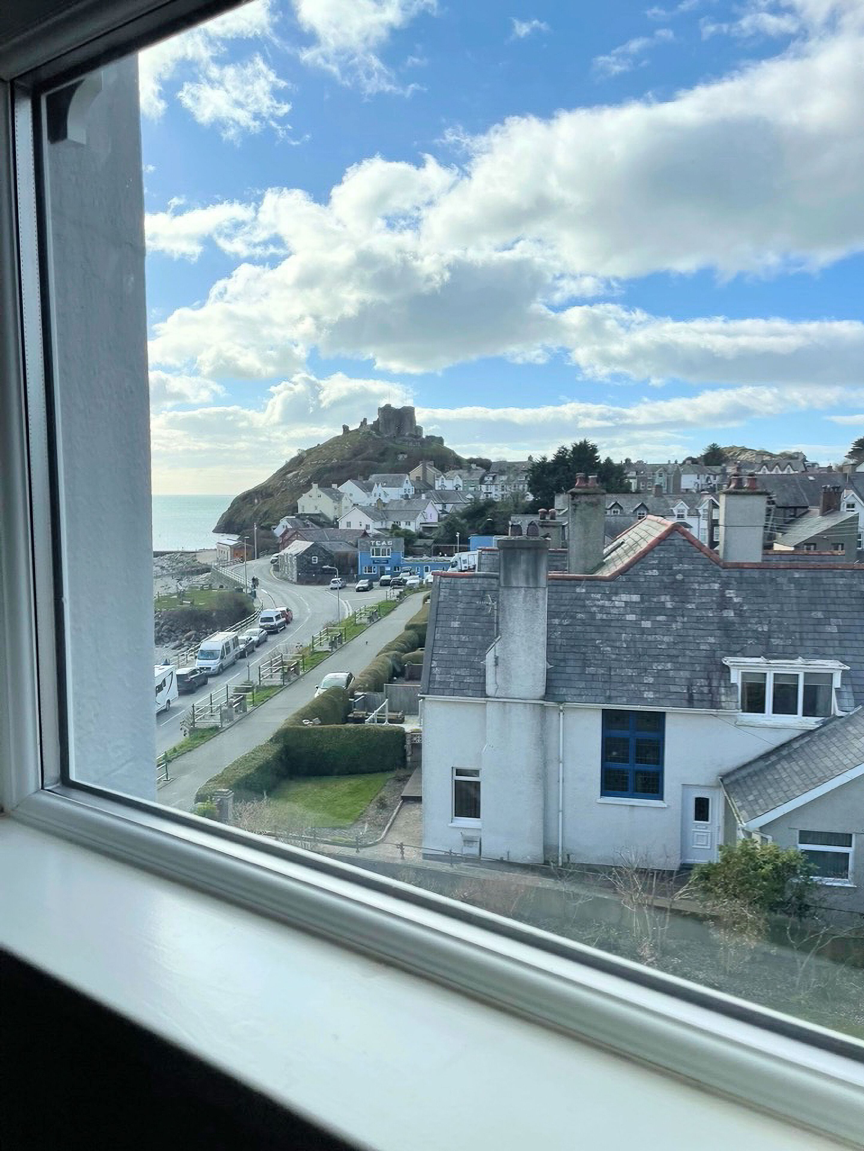 A coastal town with a prominent hilltop structure, residential buildings, and a road with parked vehicles.