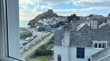 A coastal town with a prominent hilltop structure, residential buildings, and a road with parked vehicles.