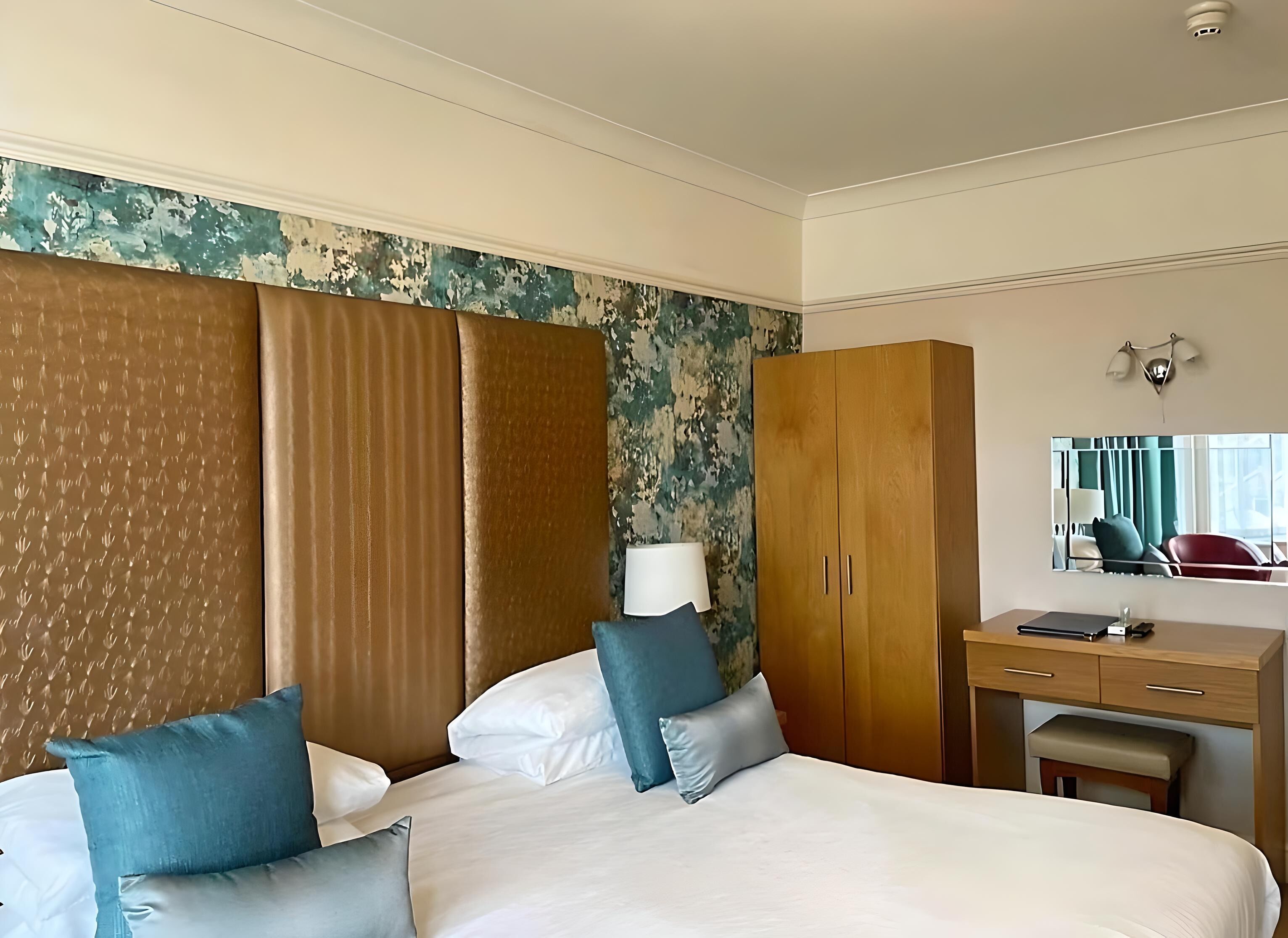 A hotel room with two beds, a wooden wardrobe, a desk with a chair, and a large mirror.