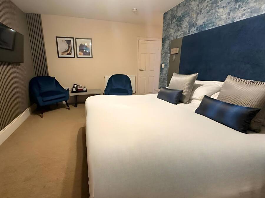 Habitación de hotel con una cama grande, dos sillas azules, un escritorio y un televisor montado en la pared.