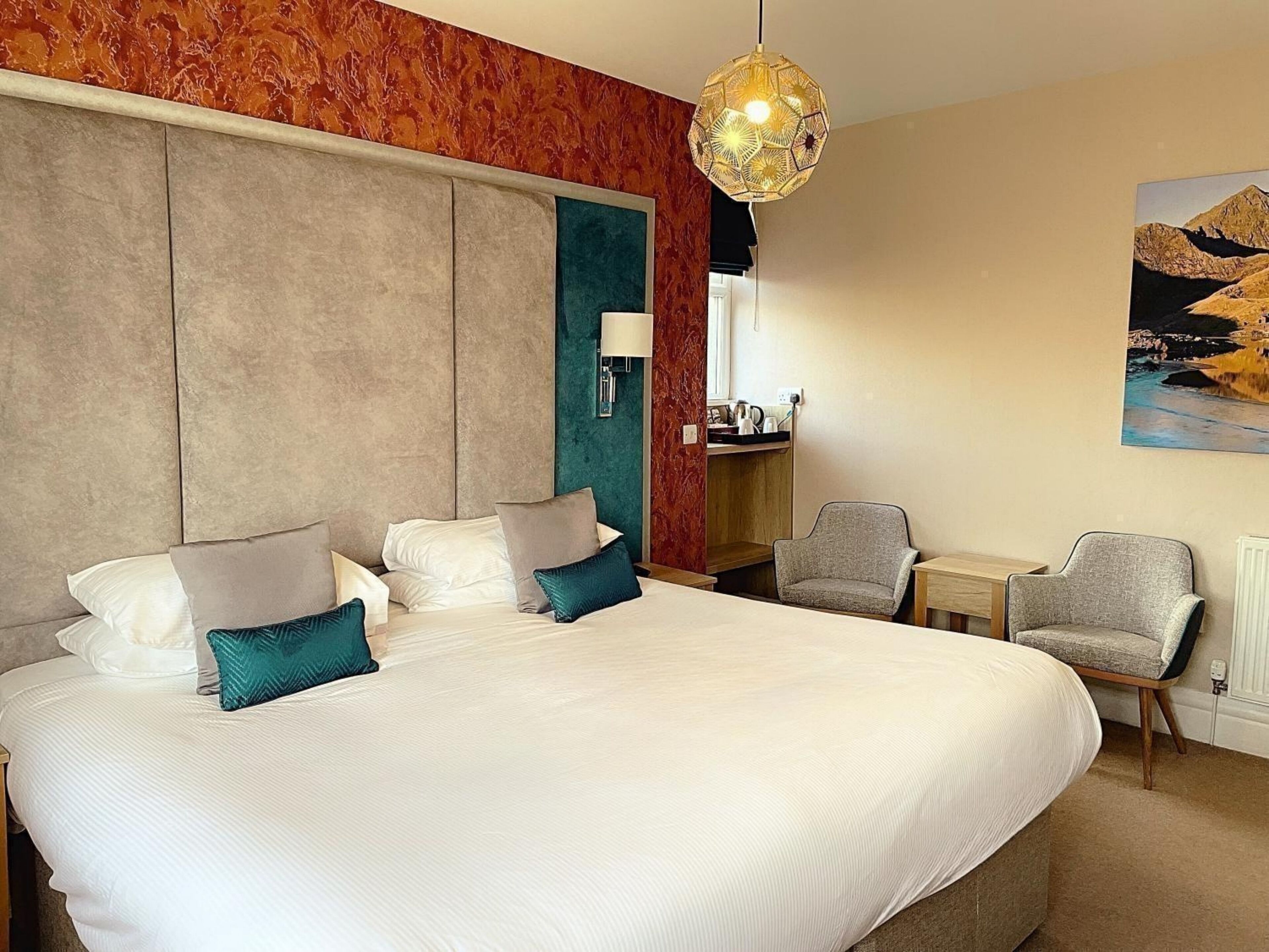 A hotel room with a large bed, two armchairs, a small table, and a painting on the wall.