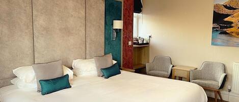 A hotel room with a large bed, two armchairs, a small table, and a painting on the wall.