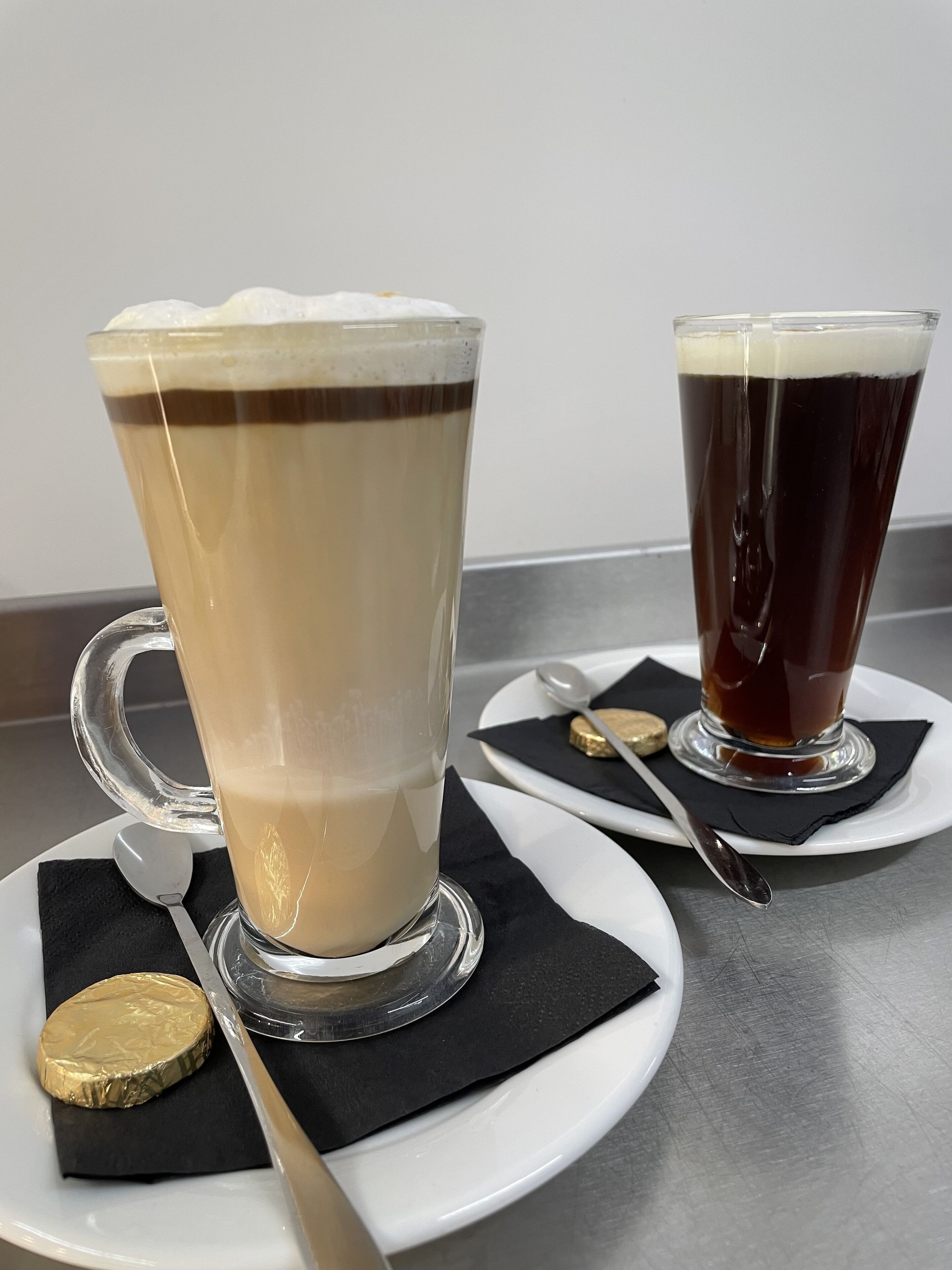 Dos vasos de bebidas sobre platos blancos con servilletas negras y una cuchara.