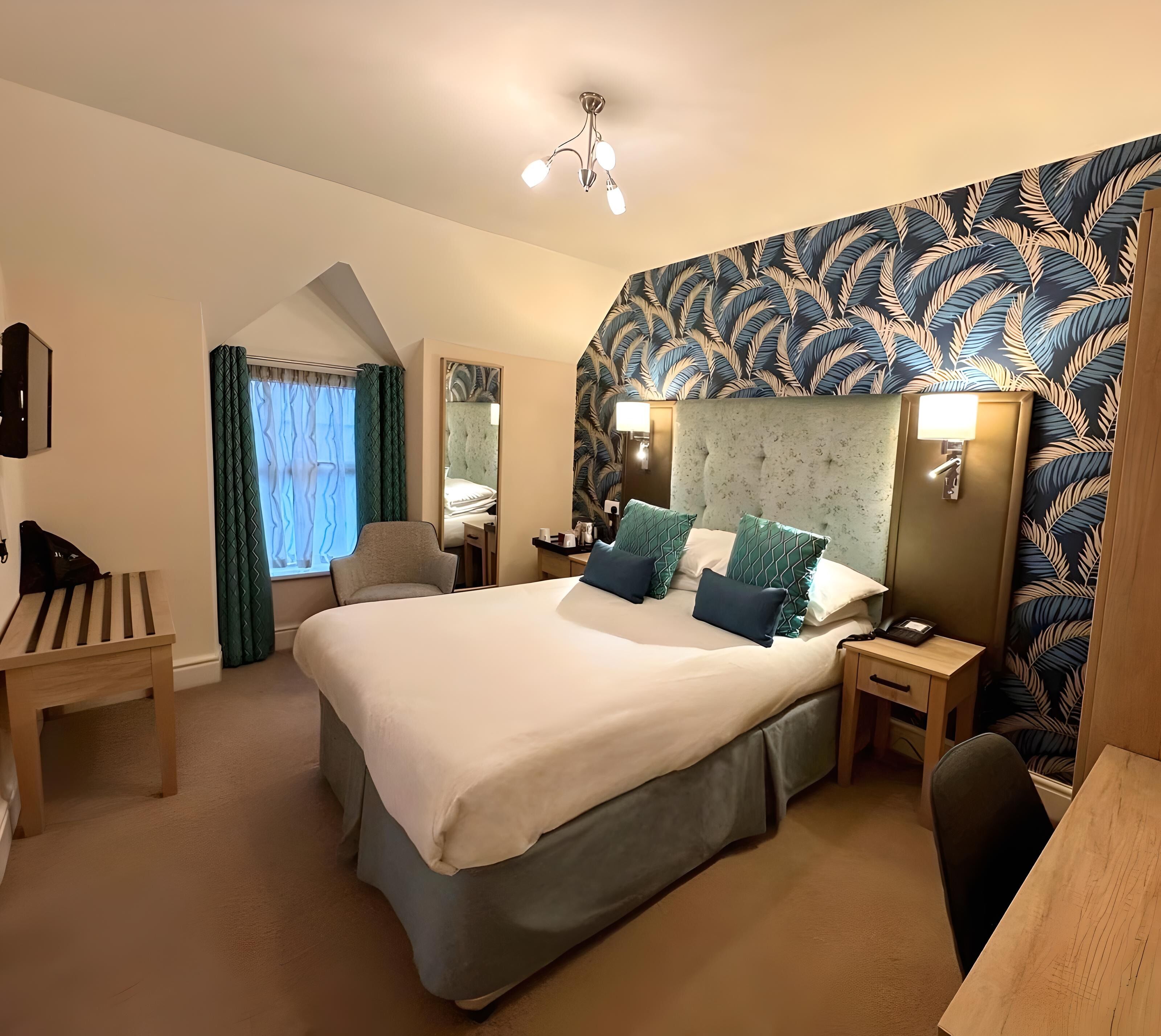 Habitación de hotel con una cama grande, un escritorio, una silla, un espejo y una pared con diseño.