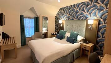 A hotel room with a large bed, a desk, a chair, a mirror, and a patterned wall.