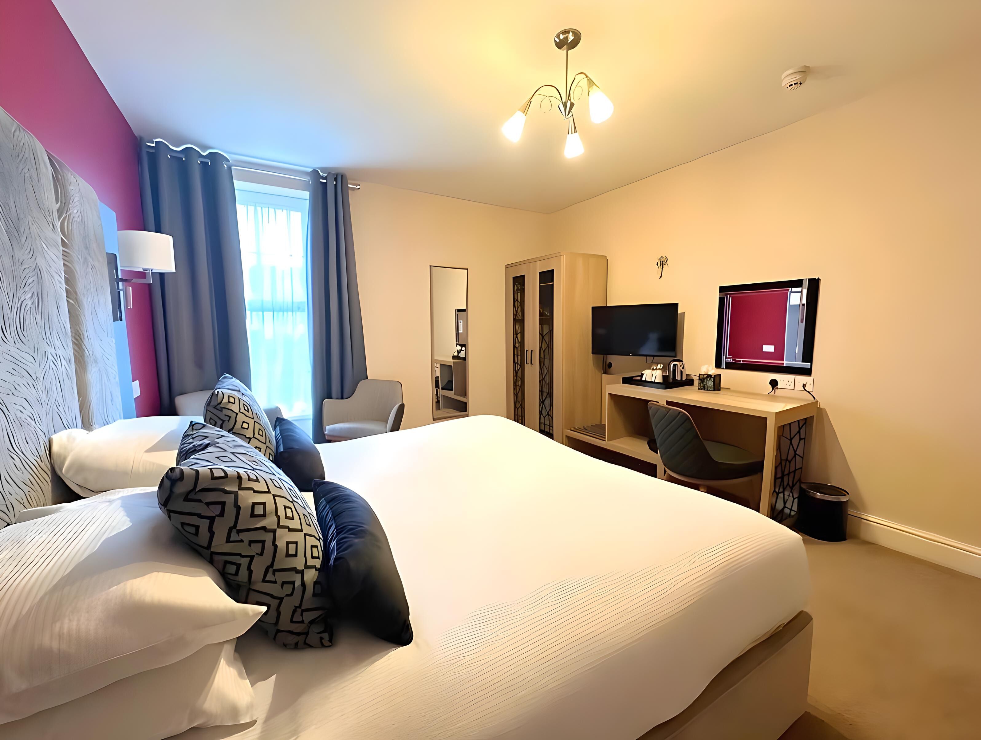 A hotel room with a bed, a desk, a chair, a TV, and a wardrobe.