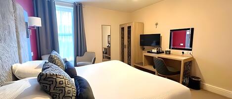 Una habitación de hotel con cama, escritorio, silla, televisor y armario.