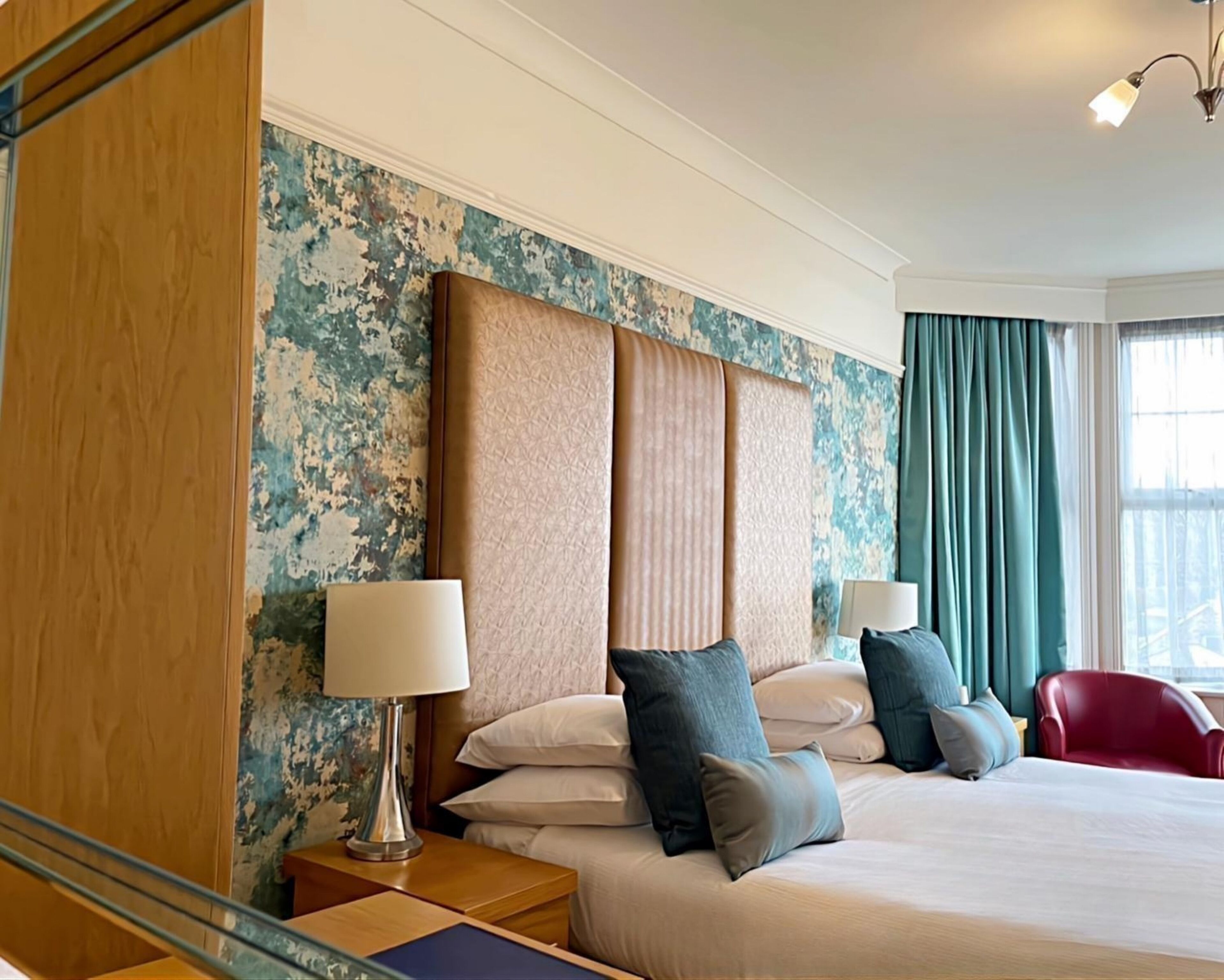 A hotel room with a large bed, a wooden headboard, a nightstand with a lamp, and a red chair.