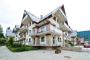 A multi-story residential building with balconies, a stone foundation, and a cobblestone driveway. - Apartamenty Sun & Snow Centrum Zakopane (Zakopane)