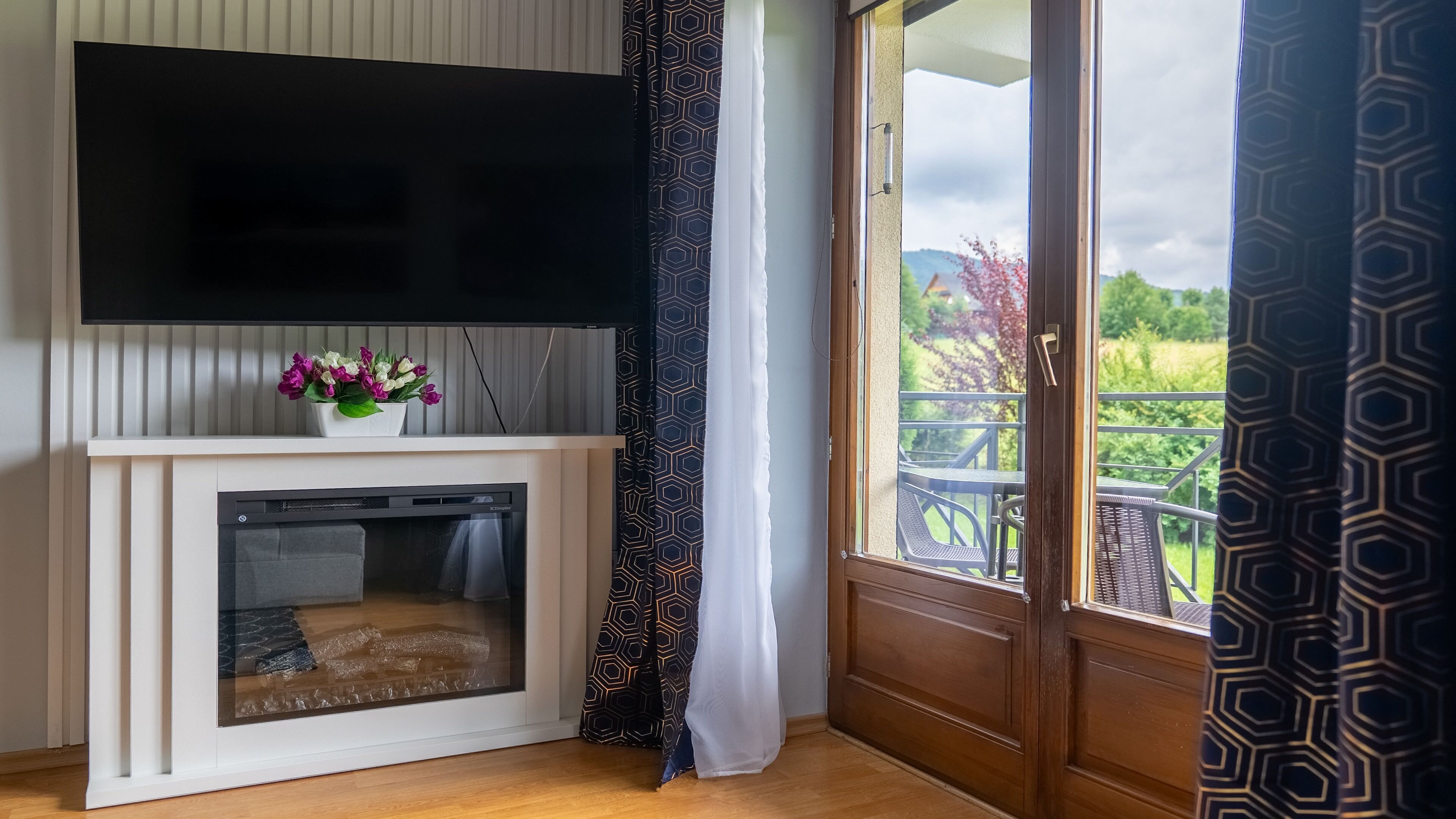 Quarto com lareira, televisão de tela plana acima e vista para uma varanda com mobiliário externo.