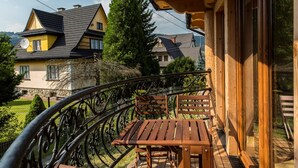 Un balcón con mesa y sillas de madera, con vista a una zona residencial con casas y árboles.