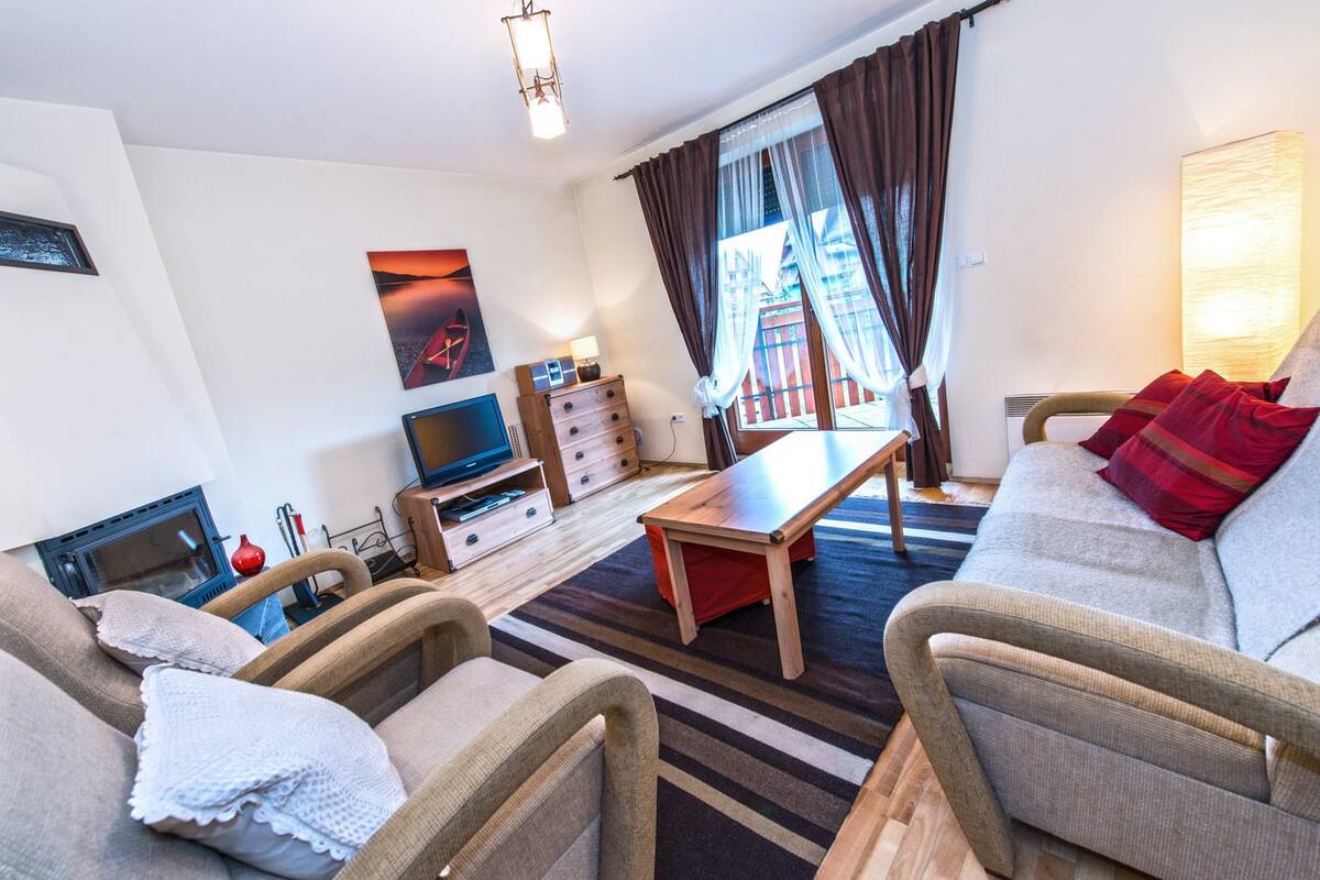 Un salon avec un canapé, des fauteuils, un téléviseur, une cheminée et une fenêtre avec des rideaux.