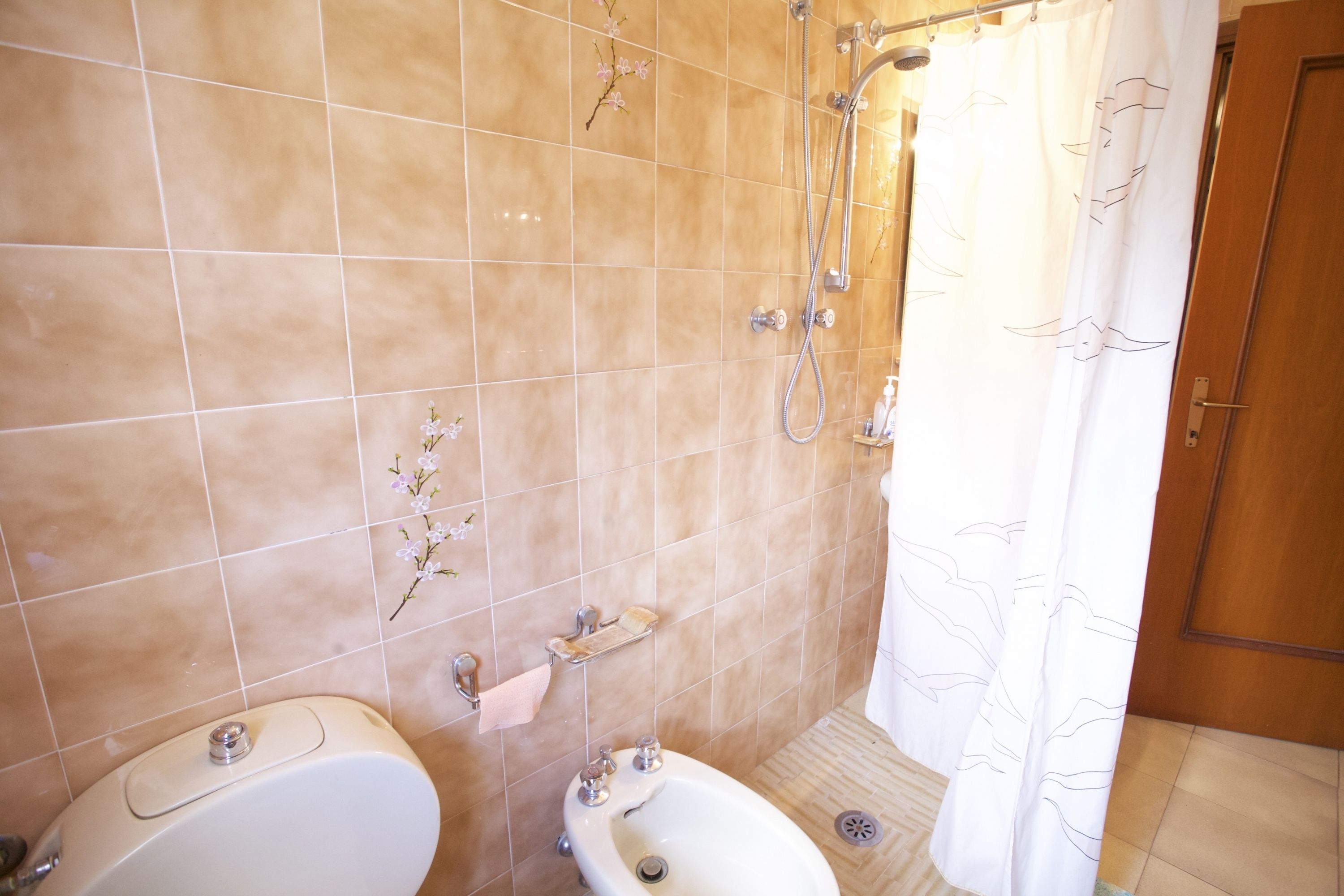 Un bagno con piastrelle color beige, una doccia, un WC e un bidet.