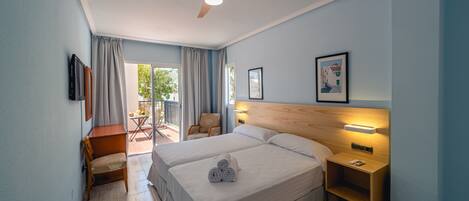 Habitación de hotel con dos camas, un ventilador de techo, una mesita de noche, una silla y vistas al exterior.