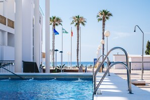 Una piscina con vistas al mar, palmeras y banderas.
