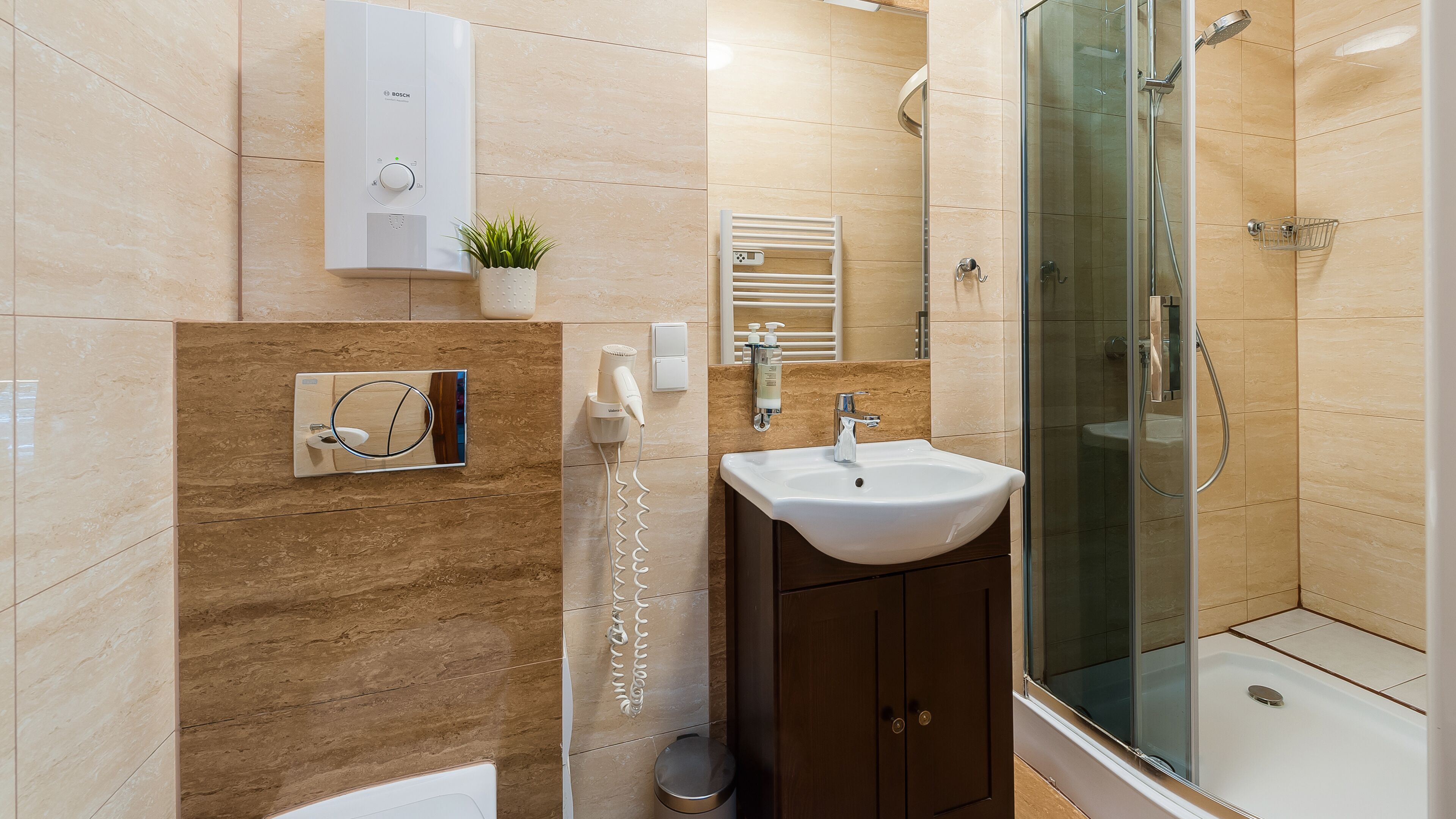 A modern bathroom with a Bosch water heater, a hairdryer, a sink, a mirror, and a glass-enclosed shower.