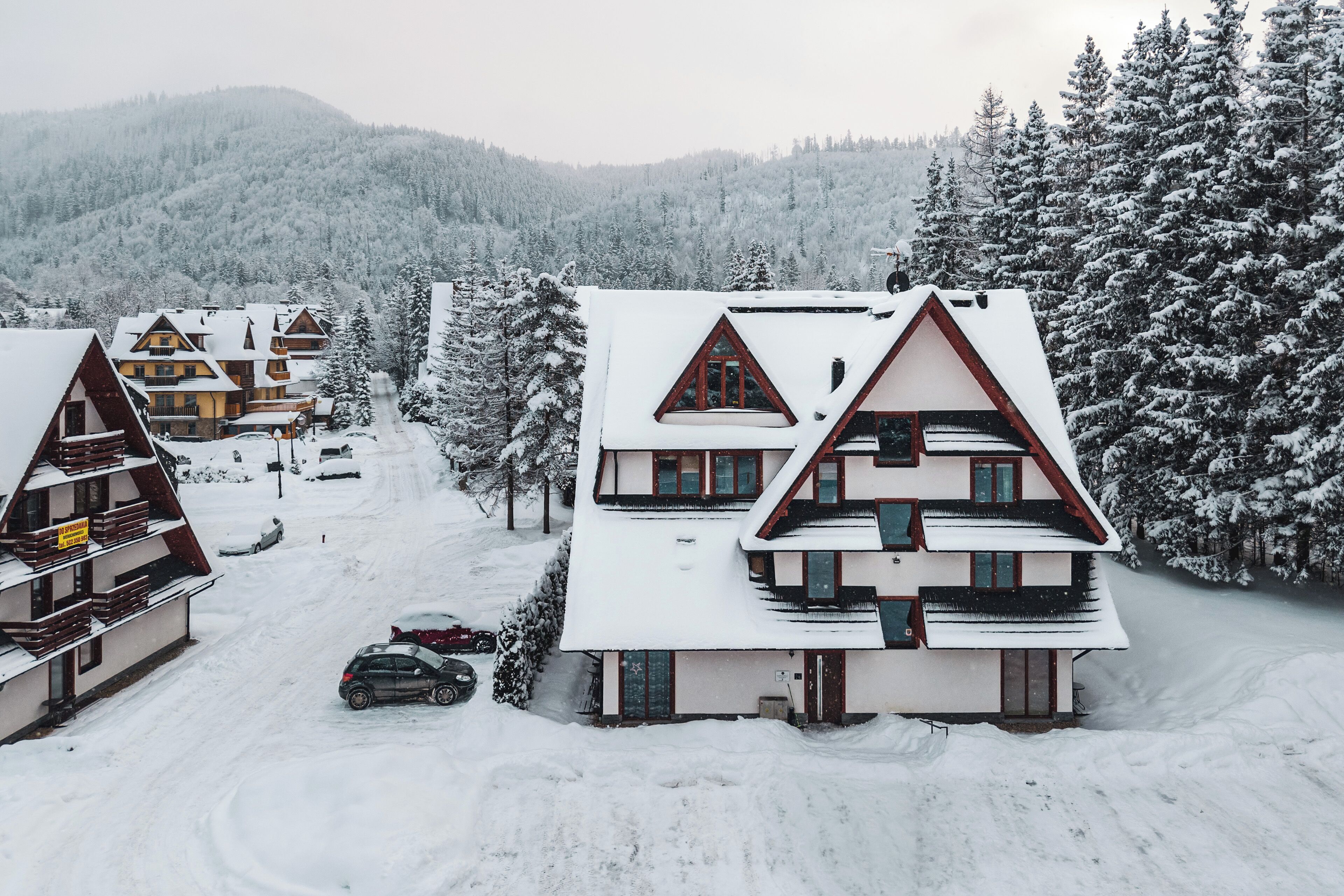 Un villaggio innevato con edifici in stile chalet, cielo sereno e montagne boscose sullo sfondo.