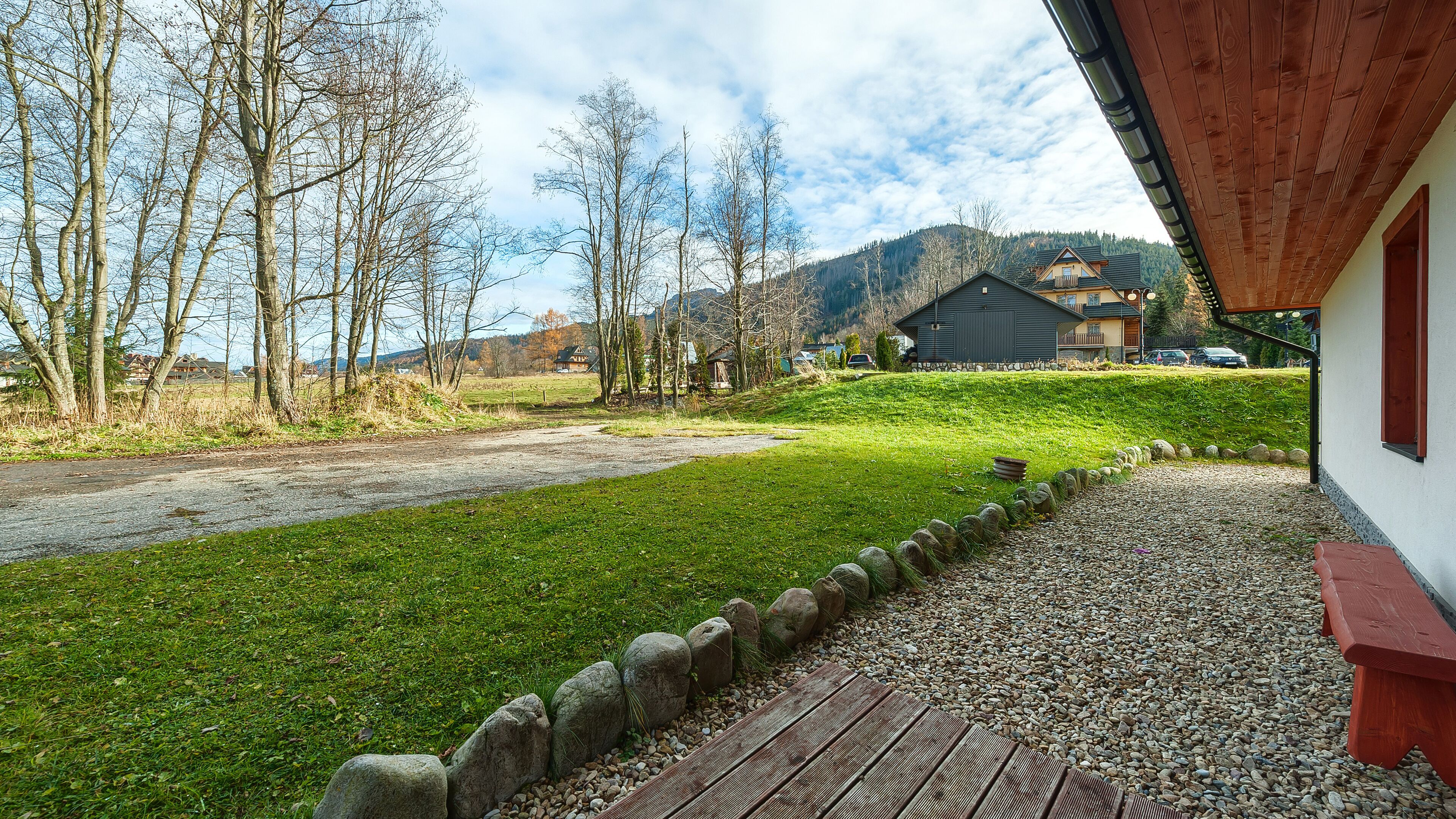 A wooden deck with a gravel path, a grassy area, and a view of a mountain and buildings in the background.