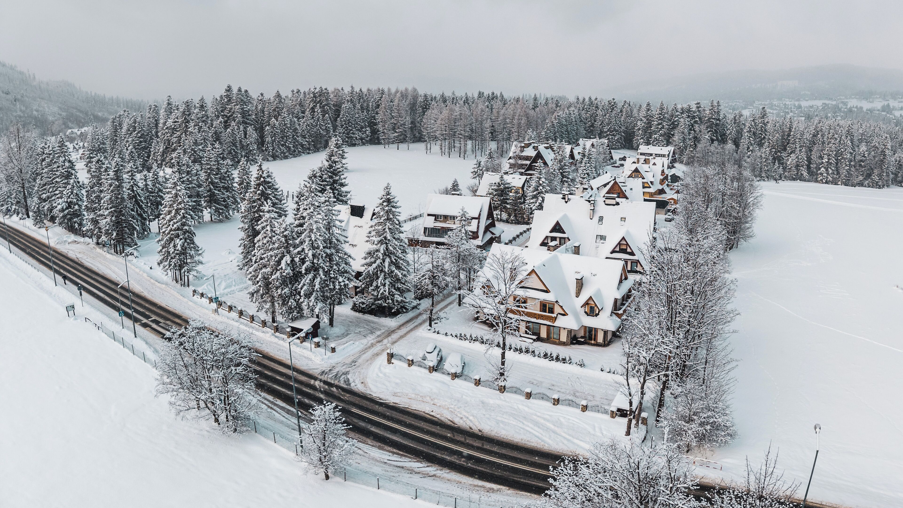 Un chalet enneigé composé de plusieurs bâtiments, entouré d’une forêt dense et traversé par une voie ferrée.