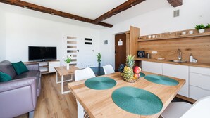Un salon moderne avec une table à manger en bois, des chaises blanches, un canapé en cuir et un téléviseur.