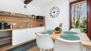 Une cuisine moderne avec un plan de travail en bois, des armoires blanches, une horloge noire et un coin repas comprenant une table en bois et des chaises blanches.
