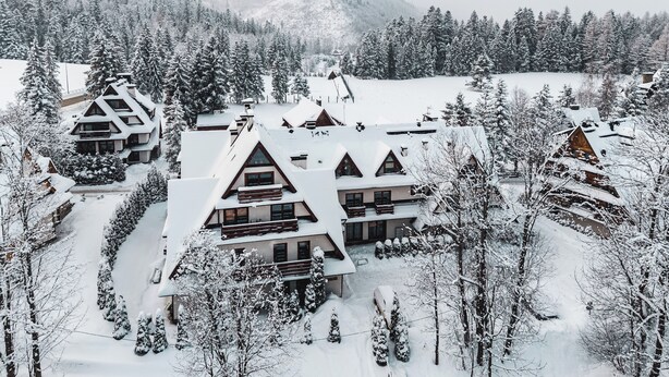 Un chalet enneigé composé de plusieurs bâtiments, entouré d’arbres et d’un paysage hivernal.